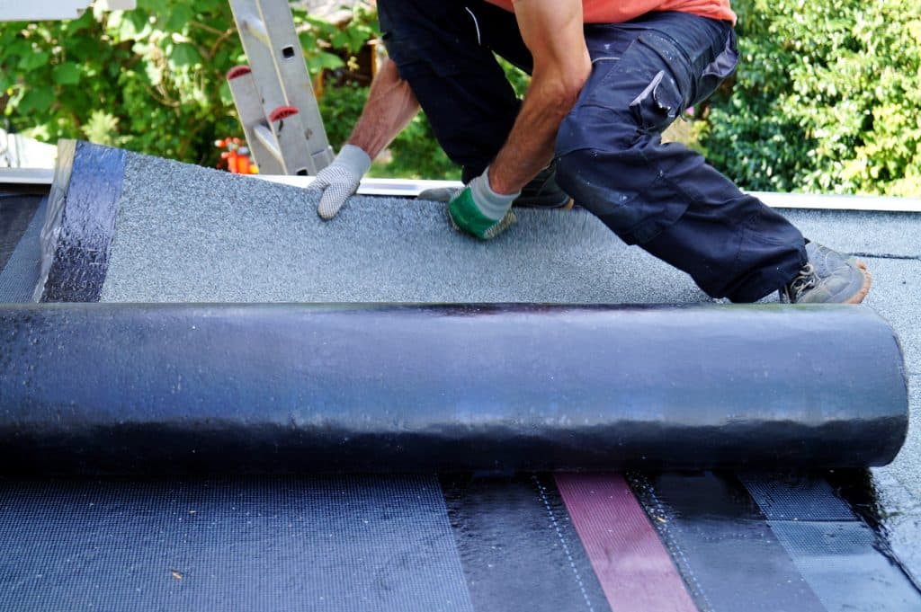 worker installing tar foil on the rooftop of building. Flat roof installation. Waterproof system by gas and fire torching.