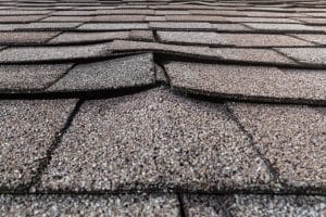 A close-up of a buckled residential asphalt shingled roof