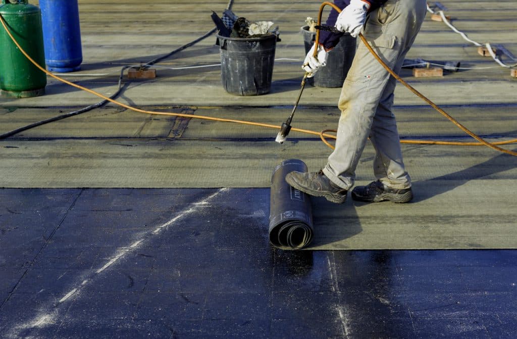 Worker preparing part of bitumen roofing felt roll for melting by gas heater torch flame. On the back of the sheath there is the stamp "Made in Italy" product