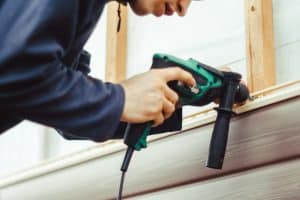 A worker installs panels beige siding on the facade of the house