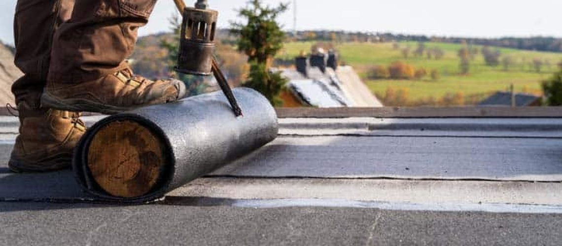 Worker Heating and melting bitumen roofing Flat roof installation.