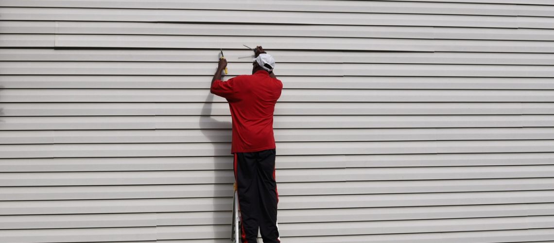 An African-American man on a ladder and fixing vinyl siding on a house