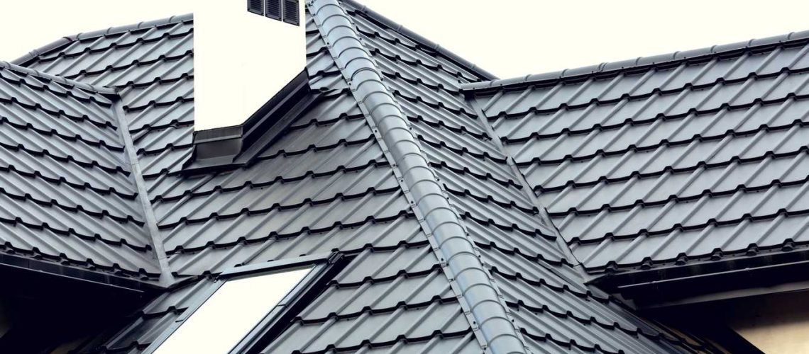 Roof of a new house with slants, a skylight, a plastered chimney and ventilation grilles. Roof covering with steel tiles.