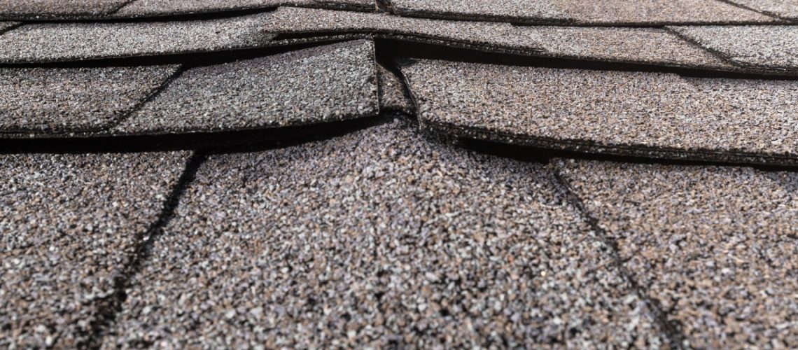 A close-up of a buckled residential asphalt shingled roof